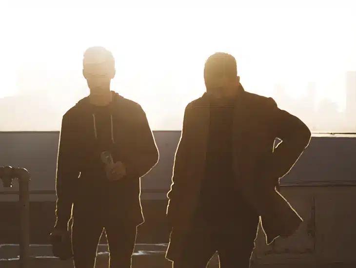 Two men standing on a rooftop with a view of the city while reading a letter from Symphonic's CEO.