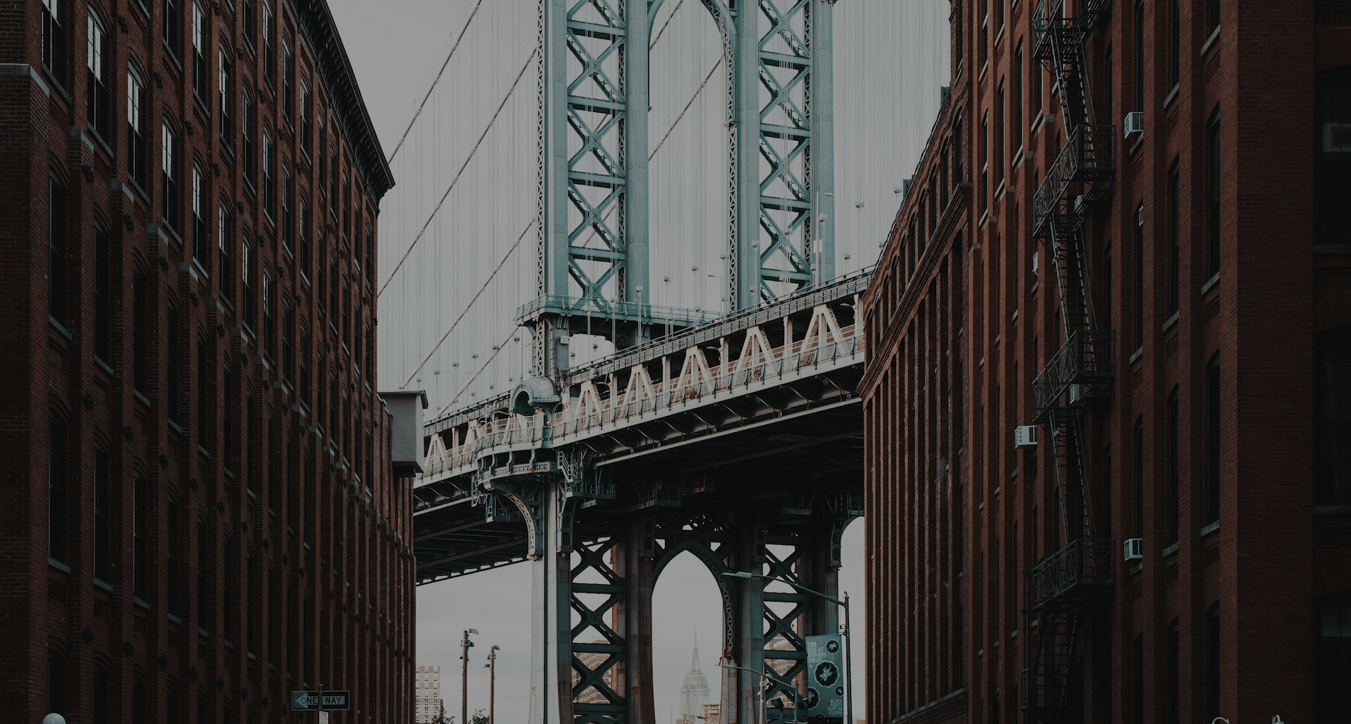 View of a bridge framed between two brick buildings on a cloudy day, with the distant skyline visible underneath—it's almost like a scene from About Symphonic, where every element harmonizes perfectly.